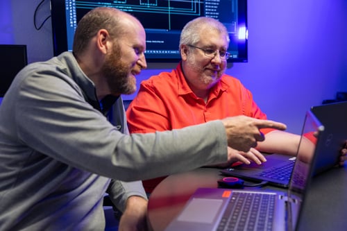 Two Frontline Communications team members working together while pointing at a laptop.