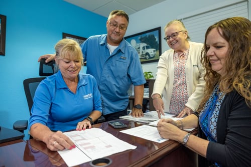 Four Frontline Communications team members gathered around a desk doing paper work.
