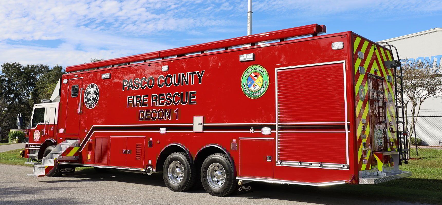 A red mobile decontamination unit is parked in front of a manufacturing facility with a blue sky background. 
