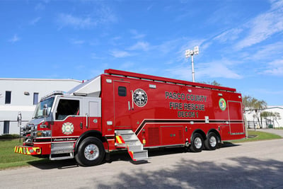 A red mobile decontamination unit is parked in front of a manufacturing facility with a blue sky background.