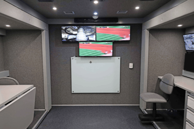 The interior of a Mobile Command Vehicle showing a back wall with three monitors and a white board.