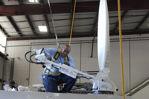 A man wearing a safety harness on top of a Frontline Communications vehicle.