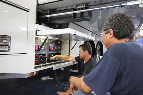 Two men servicing the inside compartment of a Frontline Communications vehicle.