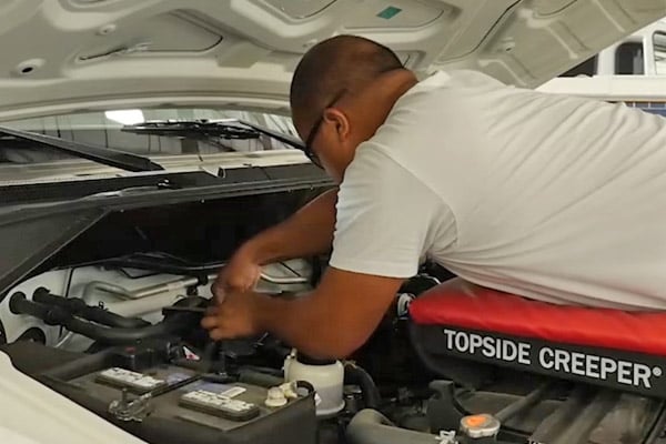 A man servicing under the front hood of a Frontline Communications vehicle.