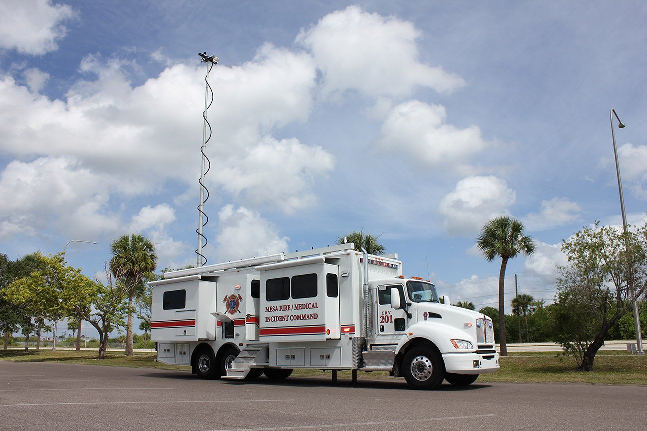 Frontline Communications white Mobile Command vehicle parked outside near trees on a cloudy day.