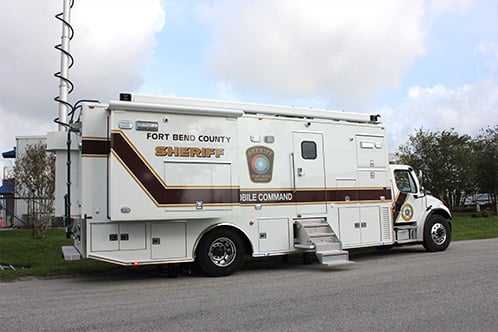 Frontline Communications white Mid-Size Mobile Command vehicle for Fort Bend County Sheriff's Office parked outside in front of the building on a cloudy day.