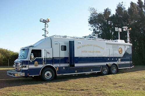 Frontline Communications Federal Mobile Command vehicle parked outside in the grass near trees on a sunny day. 