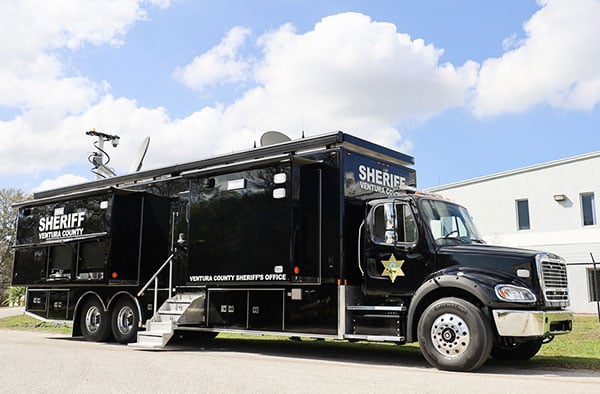 Frontline Communications black Large Mobile Command vehicle for Venture County Sheriff’s Office parked outside the building on a cloudy day. 