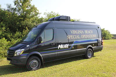 A black hostage negotiation vehicle with words 'Virginia Beach Special Operations' is parked on the grass with green trees and sky in the background.