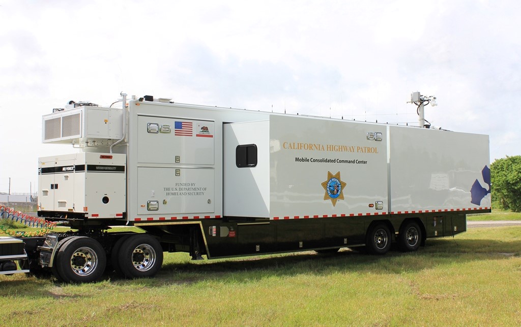 The white California Hwy Patrol Frontline Mobile Command Trailer is parked in a grassy field.