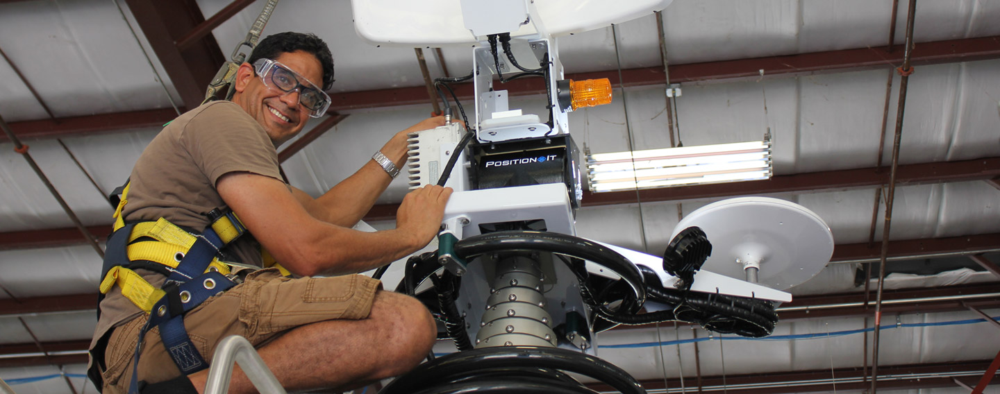A man in a harness working on a satellite in the Frontline Communications building.