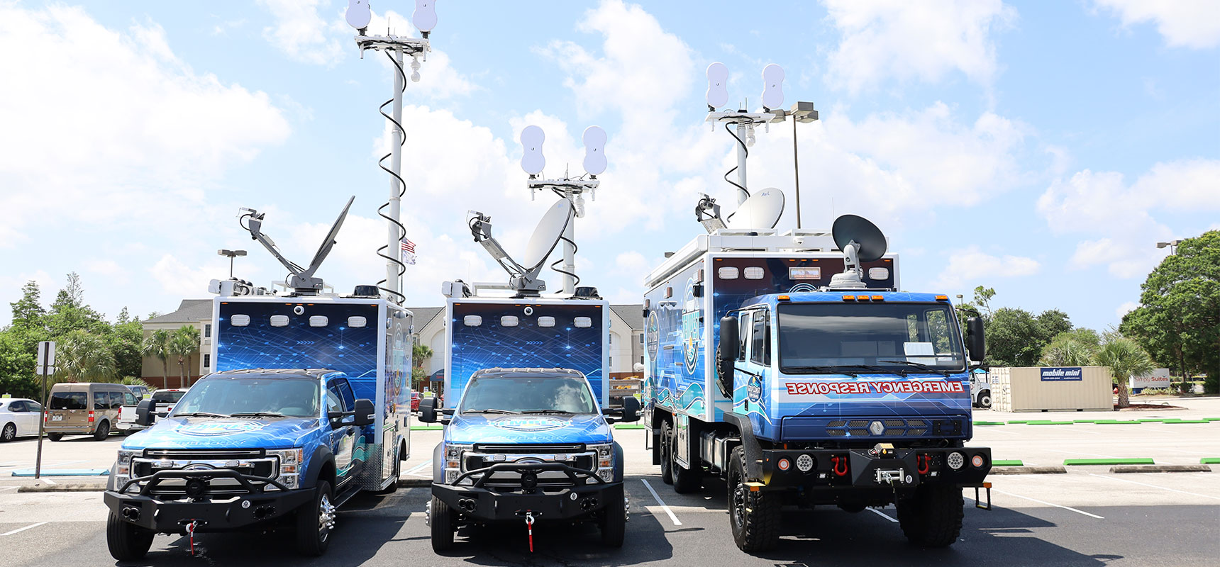 Three Frontline Communications vehicles parked outside in the parking lot on a sunny day.