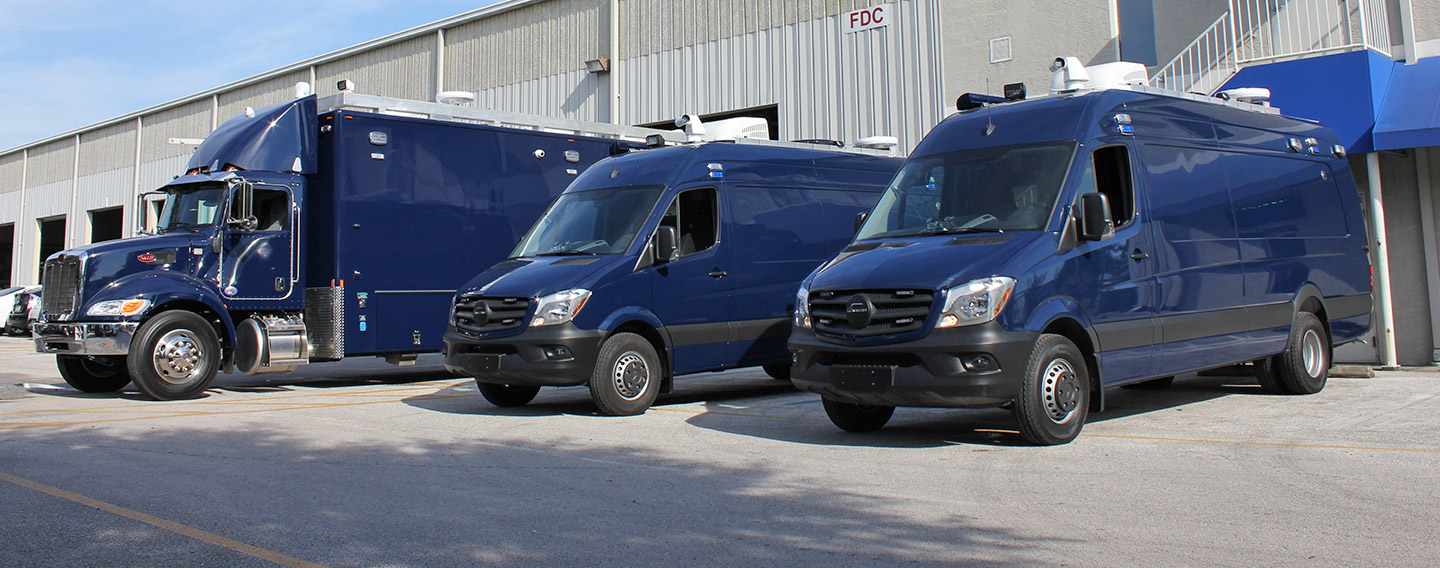 Three blue Mobile Precinct vehicles parked outside in front of the Frontline Communications building on a sunny day. 